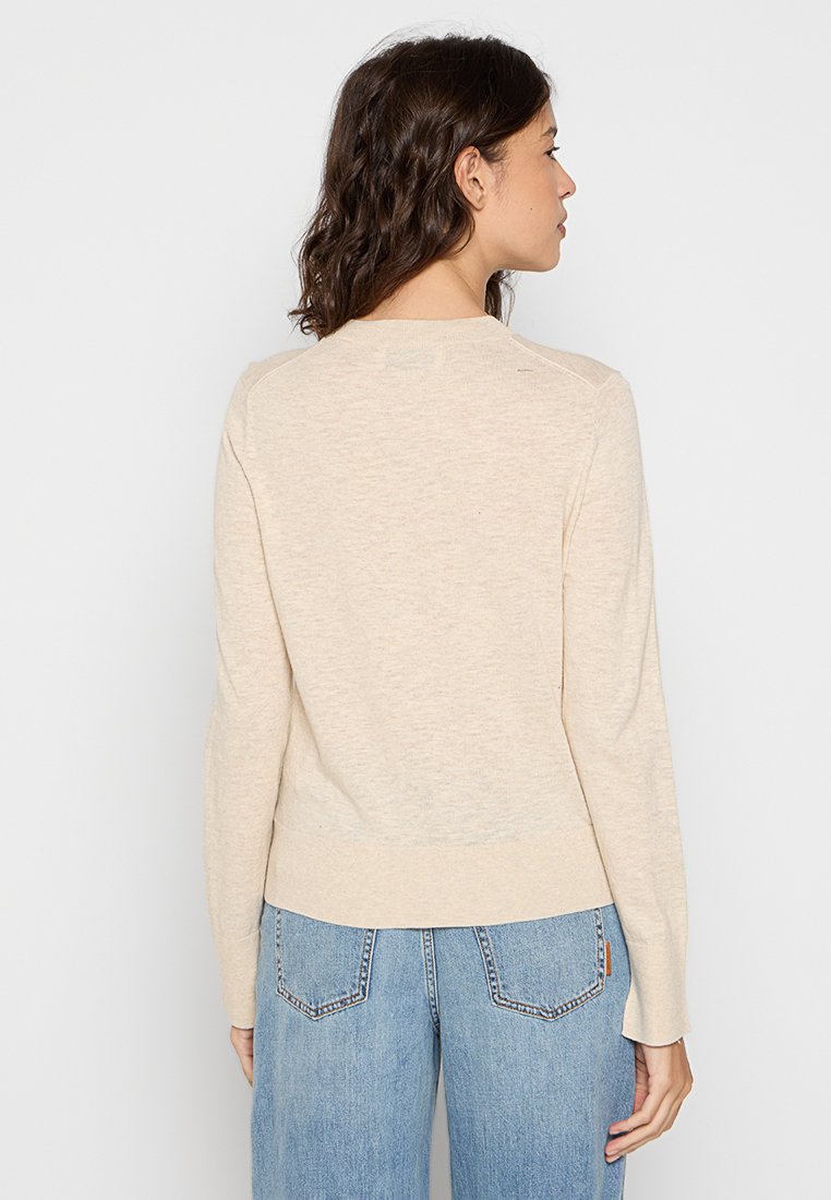 Jasnobeżowy sweter dzianinowy z długimi rękawami, okrągłym dekoltem i dopasowanym w talii. Gładka faktura i minimalne detale. Pokazany widok z tyłu.