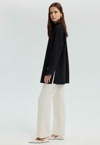 Black long-sleeve shirt with side slits, paired with white wide-leg trousers and pointed-toe shoes, featuring a smooth texture.