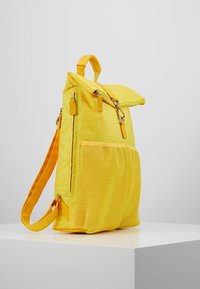 Mochila de tela amarilla con un bolsillo lateral de malla, compartimentos con cremallera, correas ajustables y una tapa plegable. Superficie texturizada y diseño ligero.