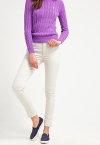 Lila kabelstickad tröja, vita slim fit-jeans och marinblå slip-on-skor. Anmärkningsvärda detaljer inkluderar ribbade muddar och en diskret logotyp på tröjan.