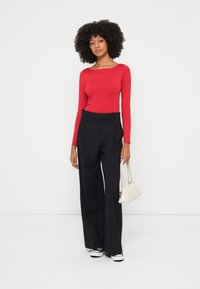 Piros bordázott hosszú ujjú felső, fekete magasderekú, bőszárú nadrággal párosítva. A modell egy kis fehér kézitáskát tart. A megjelenést fekete sportcipő egészíti ki.