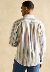 Rööbastega pikkade käistega särk kerge kangaga, millel on horisontaalsed vikerkaare rööpad, nööpidega krae ja selja voldid. Kreemjas alusvärv.