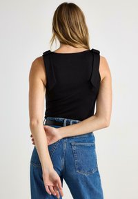 Sort ærmeløs top med brede skulderstropper, kombineret med højtaljede blå denimjeans med klassisk fem-lomme-design.