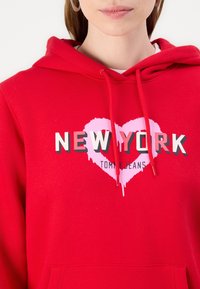 Červená mikina s kapucňou so grafickým potlačou "NEW YORK" a ružovým srdcom. Materiál je mäkký, s prednou vreckom a nastaviteľnými šnúrkami na kapucni.