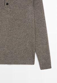 Szary sweter z dzianiny z okrągłym dekoltem, pojedynczym ciemnym guzikiem, ściągaczami na mankietach i w dolnej części. Miękka faktura z lekko melanżowym wykończeniem.