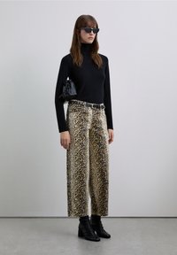 Haut à col roulé noir, pantalon large à imprimé léopard beige et noir, ceinture noire et bottines noires à talons. Accessoires : lunettes de soleil noires et sac.