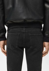 Schwarze Denim-Jeans mit mittlerer Leibhöhe, ausgestattet mit zwei Gesäßtaschen, dezenten Steppnähten und einem glatten Abschluss am Bund.