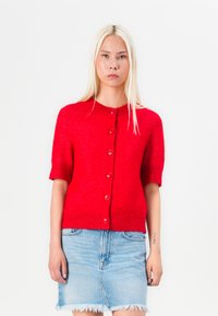 Rode cardigan met korte mouwen, gemaakt van een gestructureerde stof, met een ronde halslijn en zes knopen aan de sluiting. Draag het over een spijkerrok.