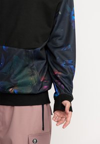 Felpa nera e multicolore con stampa floreale e galattica sulle maniche e sul retro. Presenta fori per i pollici nei polsini, materiale morbido.