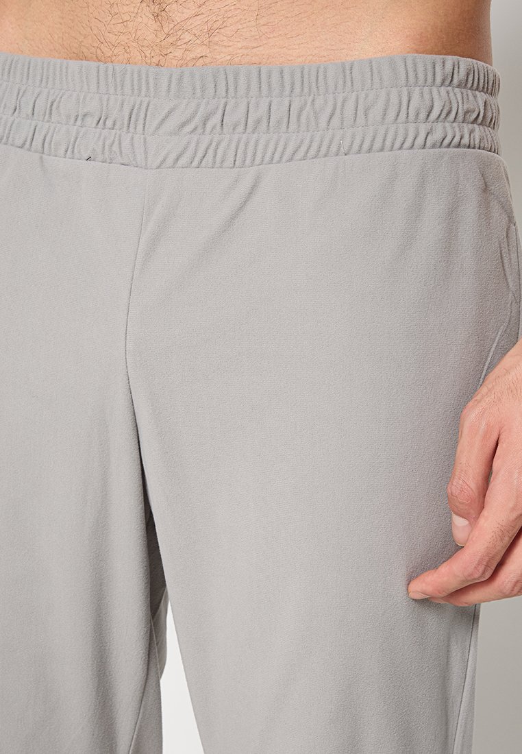 Primo piano della vita e della mano di un uomo che indossa pantaloni con elastico in vita di colore grigio chiaro, con una tasca laterale visibile.