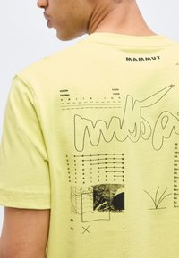 Άτομο που φοράει ανοιχτό κίτρινο T-shirt της Mammut με μαύρη αφηρημένη γραμμή τέχνης, κείμενο και γραφικά τύπου διαγράμματος στην πλάτη.