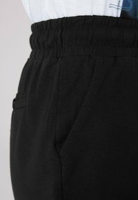 Zwarte katoenen joggers met een verzamelde tailleband, zijzakken en een gladde textuur. Geen zichtbare patronen of accenten.