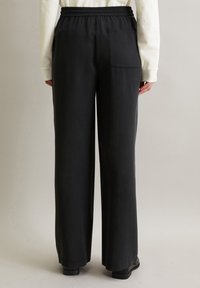 Schwarze weit geschnittene Hose mit elastischem Bund und einer einzelnen Gesäßtasche. Der Stoff wirkt glatt mit mattem Finish.