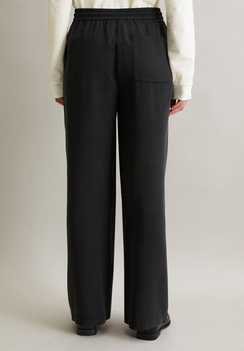 Schwarze weit geschnittene Hose mit elastischem Bund und einer einzelnen Gesäßtasche. Der Stoff wirkt glatt mit mattem Finish.