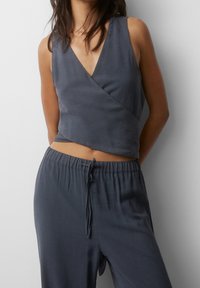 Grijze wikkelstijl mouwloze top gemaakt van lichte stof, gecombineerd met een bijpassende broek met trekkoord. Soepele textuur met een comfortabele pasvorm.