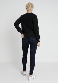 Maglione nero con maniche lunghe, polsini e orlo a coste. Abbinato a jeans skinny blu scuro con tasche posteriori e sneakers bianche.