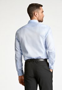 Lichtblauw overhemd met lange mouwen, een klassieke kraag, knoopmanchetten en een gladde textuur, gecombineerd met zwarte broek met achterzakken.