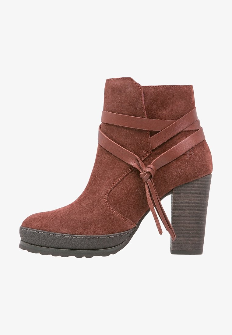 Suede ankle boot in rust color with a chunky stacked heel. Features leather straps wrapped around the boot and a round toe. Textured sole.