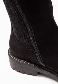 Schwarze Wildleder-Ankle-Boots mit einem strukturierten Seitenpanel, einem kontrastierenden glatten Reißverschluss und einer robusten Gummisohle mit Profil.