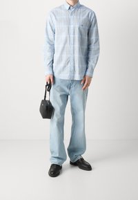 Camicetta a righe blu chiaro con bottoni, jeans blu chiaro dalla vestibilità ampia, scarpe nere e una piccola borsa nera con manico.