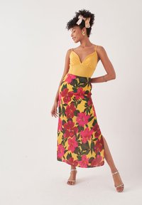 Geel bodysuit met een diepe V-hals, gecombineerd met een bloemenmaxirok met roze en groene patronen en een hoge split.