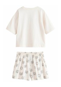 Világos krémszínű pamut rövid ujjú póló, hozzáillő rövidnadrággal, amely fekete szívmintával díszített fehér alapon.