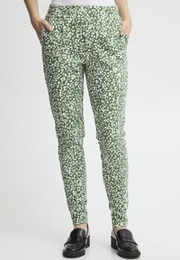 Groene, gestreepte broek met wit luipaardmotief; heeft zijzakken en een aansluitend ontwerp. Gepaard met zwarte instappers.
