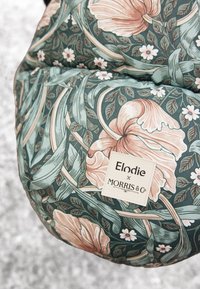 Tyyny, jossa on kukkakuvio vihreissä ja vaaleanpunaisissa sävyissä, ja joka sisältää tekstin "Elodie x Morris & Co." teksturoitua harmaata taustaa vasten.