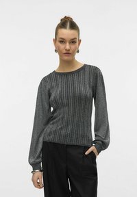 Maglione a maglia con strisce argentate, maniche lunghe e leggermente voluminose, scollatura a girocollo e vita aderente. Indossato con pantaloni neri.