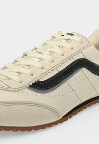 Αθλητικό παπούτσι Vans σε κρεμ αποχρώσεις με λευκά κορδόνια, μαύρη πλαϊνή ρίγα, υφασμένο πάτο και διάτρητες λεπτομέρειες στο πάνω μέρος.