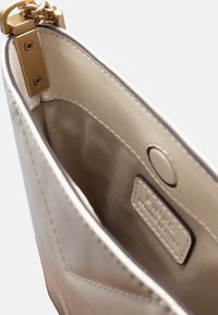 Interno di una borsa a tracolla in finta pelle beige con texture liscia, hardware dorato, chiusura magnetica e foderatura in tessuto con un'etichetta del marchio.