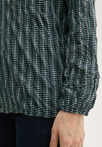 Grün gemustertes Hemd mit weißen und hellgrünen Streifen; strukturierter Stoff; geraffte Ärmel; lockere Passform; Saum am Bund gerafft.