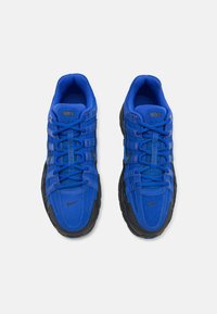 Blue Nike sneakers with black accents. Mesh and suede materials. Rounded toe, textured laces, and a distinctive sole pattern. Nike logo on tongue.