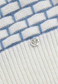 Nahaufnahme eines weißen Strickstoffs mit blauem Ziegelmuster und einer kleinen silbernen herzförmigen Metallnadel, die angebracht ist.