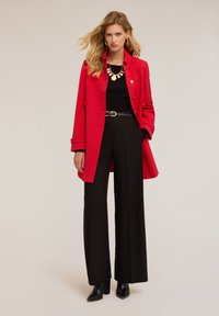 Culoare roșie, palton cu un design ajustat, top negru cu nervuri, pantaloni negri cu talie înaltă și botine negre cu toc. O brățară din aur pune în evidență ținuta.