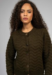 Cardigan tricoté en vert foncé avec une texture en zigzag, col rond et cinq boutons métalliques sur le devant.