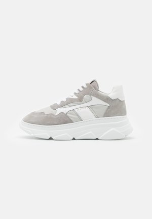 Niski sneakers z masywną białą podeszwą, jasnoszarym zamszowym i nylonowym cholewką, białymi skórzanymi akcentami oraz białymi sznurowadłami, przedstawiony na jednolitym tle.