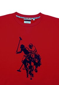 Červené bavlněné tričko s potiskem námořnického modrého polo hráče a koně. Kulatý výstřih a krátké rukávy se zesílenými švy.