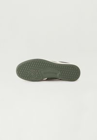 Green rubber sneaker outsole with a textured surface and patterned tread. Features logo imprint. Clean design with contrasting accents.