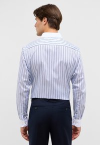 Camicia a maniche lunghe di colore azzurro chiaro con sottili righe verticali, con colletto e polsini bianchi, realizzata in tessuto liscio. La vista posteriore mostra una vestibilità sartoriale.