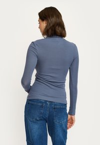 Camicia slim-fit a maniche lunghe in tessuto blu a costine, con colletto alto e texture liscia, abbinata a pantaloni in denim blu a vita alta.