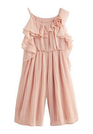 Jeune fille portant un haut rose à volants et un pantalon large plissé avec des chaussures Mary Jane beige, debout sur un sol à carreaux.