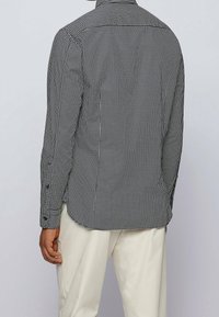 Czarna i biała koszula w kratę z długim rękawem, standardowym kołnierzem, zapinanymi na guziki mankietami oraz zaokrąglonym dołem. Tkanina wydaje się gładka i strukturalna.