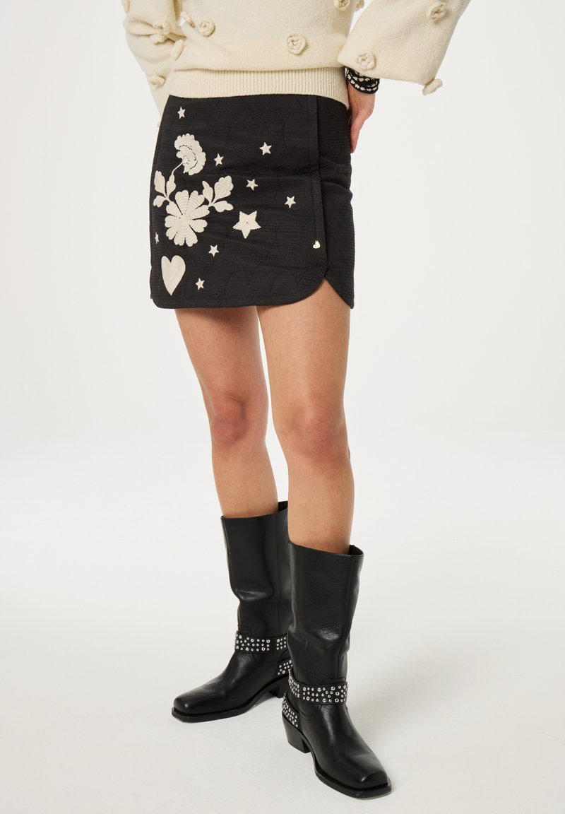 Zwarte geborduurde mini rok met bloemen- en sterrenmotieven in het wit. Gecombineerd met zwarte knie-high laarzen met studs.