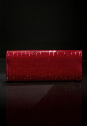Clutch in pelle rossa con texture lucida a coccodrillo, forma rettangolare e cuciture in contrasto. Design minimalista su una superficie riflettente.
