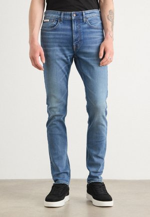 Skinny fit blauwe jeans van denim met een vervaagde was, voorzien van een vijf-pocket ontwerp en een knoopsluiting, gecombineerd met zwarte sneakers.