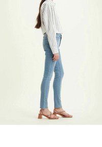 Jeans skinny de color azul claro hechos de denim, combinados con una camisa blanca a rayas y sandalias de tacón con tiras color beige, vistos de lado.