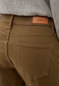 Brązowe bawełniane spodnie z naszywaną kieszenią i skórzaną metką w pasie. Posiadają prosty krój i solidne szwy.