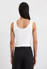 Witte katoenen tanktop met een ronde achterkant, gecombineerd met hoge zwarte broeken met grote achterzakken. Gladde textuur, casual ontwerp.