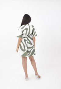 Abito bianco con motivo astratto verde, maniche corte, vita arricciata e gonna svasata. Indossato con sandali trasparenti con tacco a blocco.